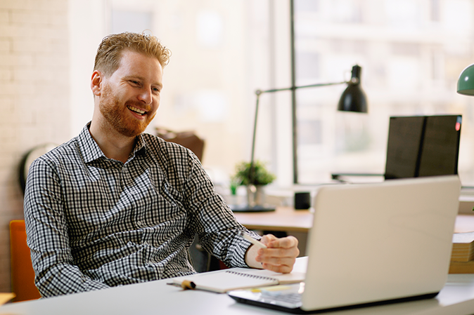 Young man smiling while looking at his laptop